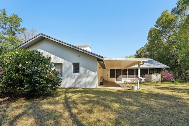 rear view of property with an attached carport, a lawn, a sunroom, and stucco siding