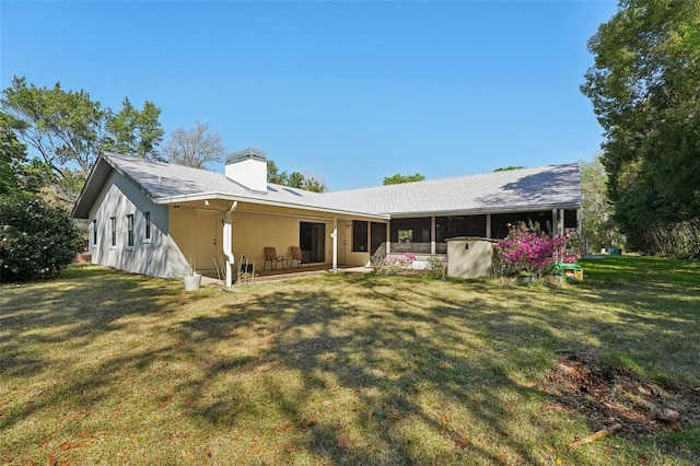 rear view of property featuring a chimney, a yard, and a sunroom