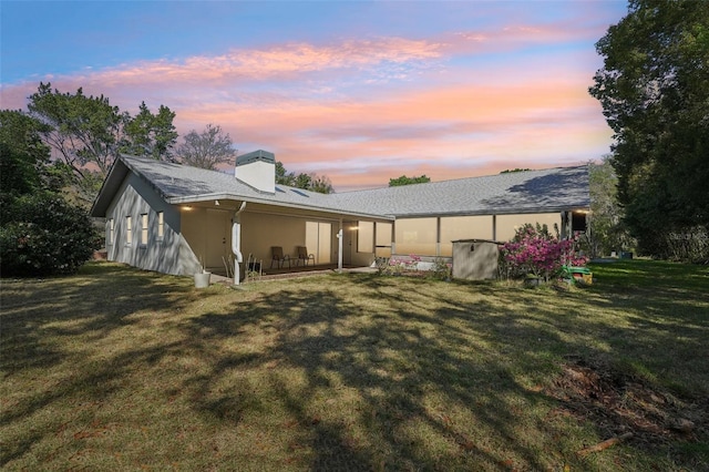 back of property at dusk featuring stucco siding, a chimney, and a yard