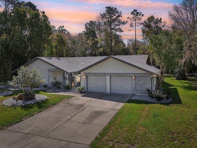 view of front of home featuring an attached garage, a shingled roof, stucco siding, a yard, and driveway