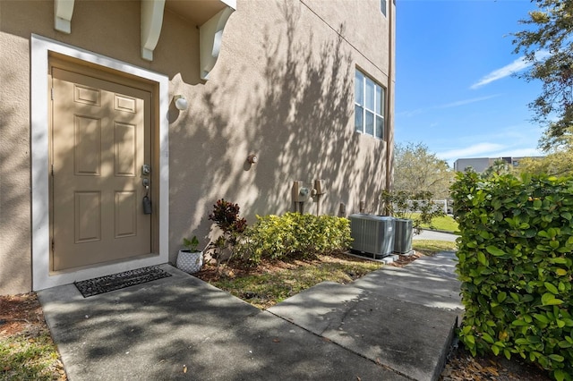 doorway to property featuring stucco siding and central AC unit