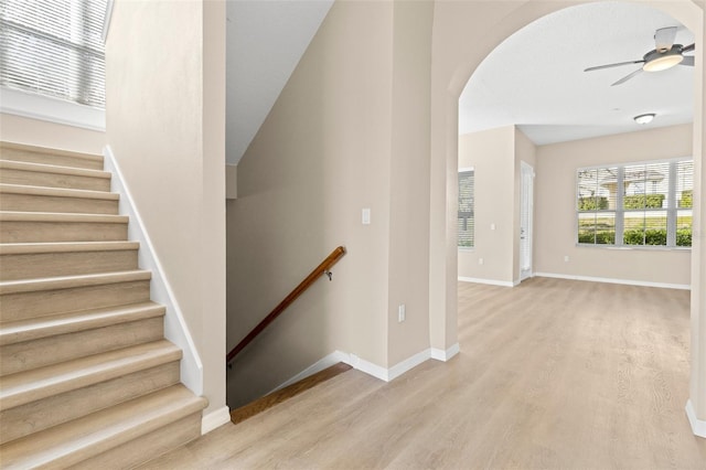 staircase with baseboards, wood finished floors, arched walkways, and ceiling fan