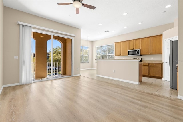 kitchen featuring light wood-type flooring, brown cabinets, a ceiling fan, appliances with stainless steel finishes, and light countertops