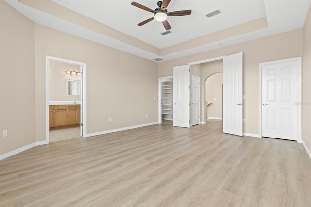 unfurnished bedroom with light wood-type flooring, a tray ceiling, baseboards, and visible vents