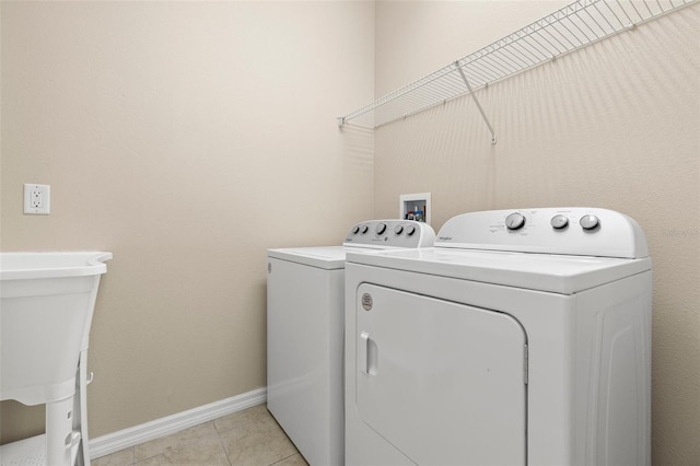 washroom featuring washing machine and clothes dryer, laundry area, baseboards, and light tile patterned flooring