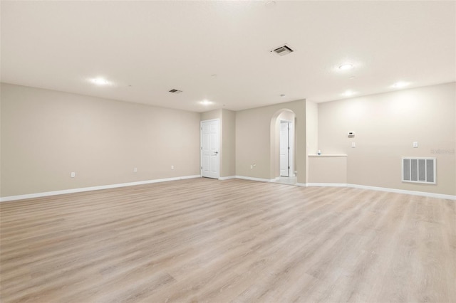 empty room featuring baseboards, arched walkways, visible vents, and light wood-type flooring