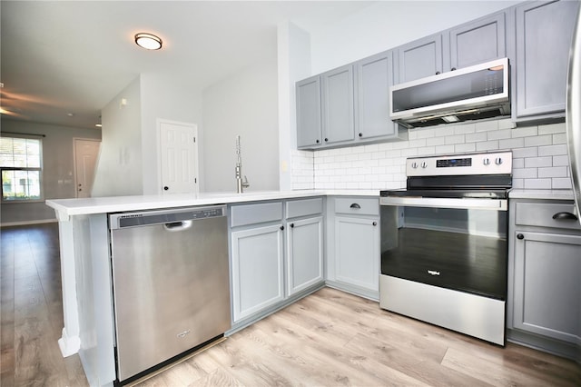 kitchen featuring decorative backsplash, appliances with stainless steel finishes, a peninsula, and gray cabinets