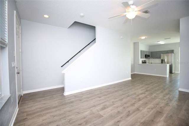 unfurnished living room featuring visible vents, a sink, wood finished floors, baseboards, and ceiling fan