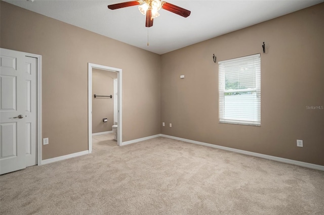 unfurnished bedroom featuring baseboards, light carpet, ceiling fan, and ensuite bath