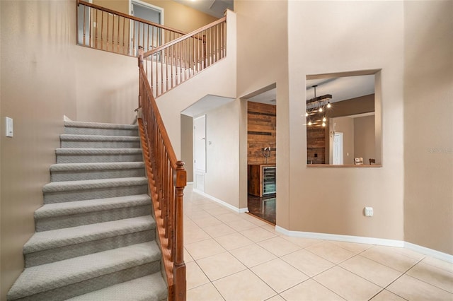 stairway featuring tile patterned floors, baseboards, a high ceiling, and wine cooler