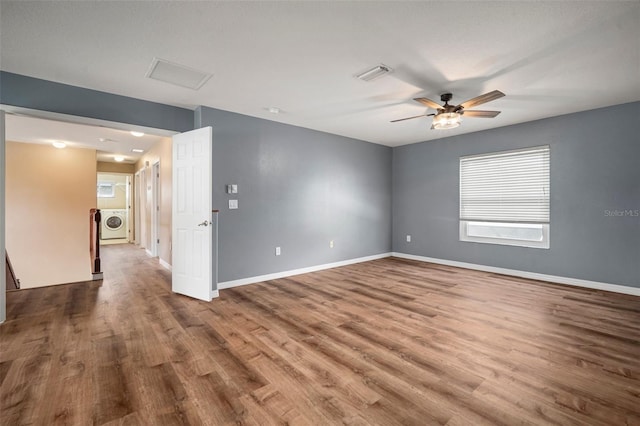 empty room featuring washer / clothes dryer, wood finished floors, visible vents, a ceiling fan, and baseboards