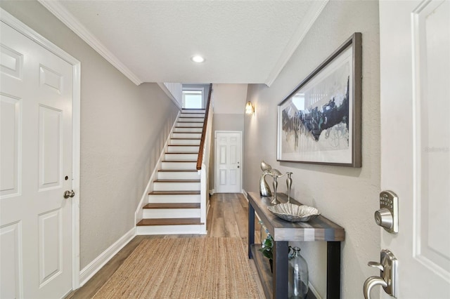 entrance foyer with ornamental molding, a textured ceiling, wood finished floors, stairway, and baseboards