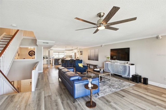 living room featuring visible vents, crown molding, baseboards, light wood-style floors, and a textured ceiling