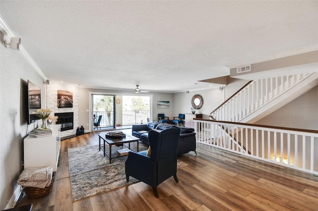 living room featuring visible vents, crown molding, a stone fireplace, wood finished floors, and a textured ceiling