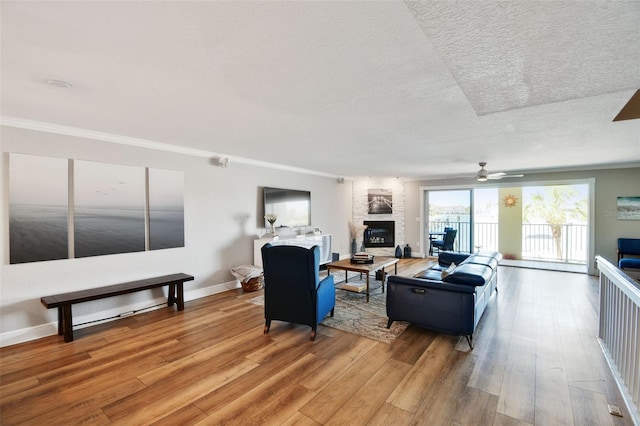 living area with a textured ceiling, wood finished floors, a stone fireplace, crown molding, and baseboards