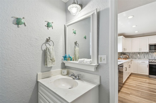 bathroom with tasteful backsplash, wood finished floors, recessed lighting, a textured wall, and vanity