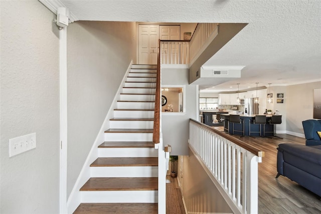 staircase with visible vents, baseboards, ornamental molding, wood finished floors, and a textured ceiling