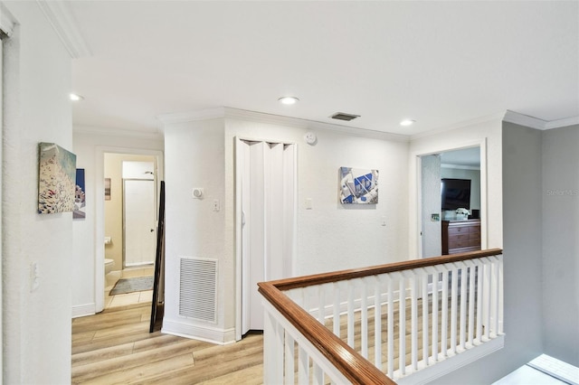 hallway with light wood-style floors, visible vents, and ornamental molding