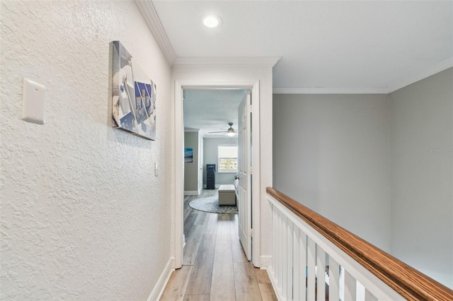 hallway with baseboards, light wood-type flooring, a textured wall, and ornamental molding