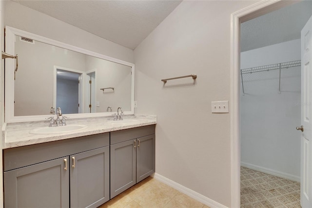 full bath featuring a sink, a walk in closet, baseboards, and double vanity