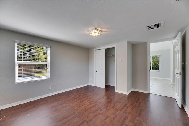 unfurnished bedroom featuring a closet, visible vents, baseboards, and wood finished floors