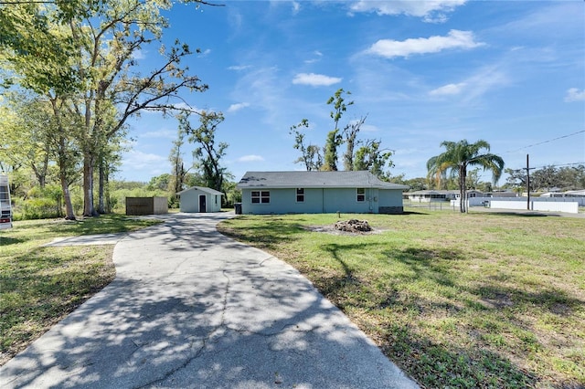 ranch-style house with fence, a front lawn, concrete driveway, an outdoor structure, and a fire pit