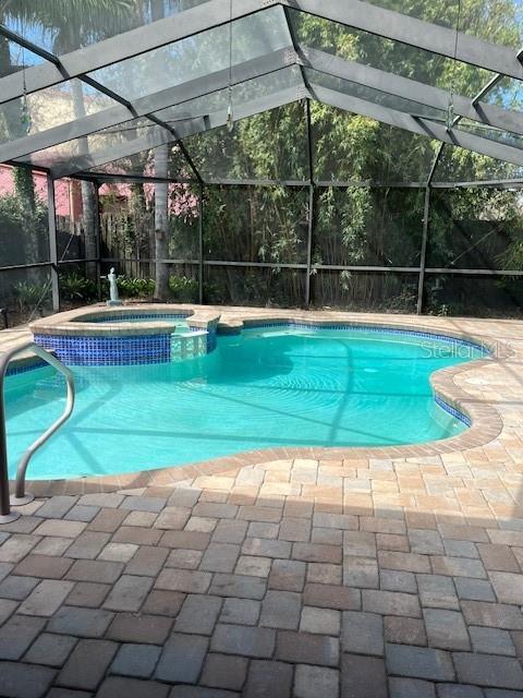 view of pool featuring a lanai, a pool with connected hot tub, and a patio