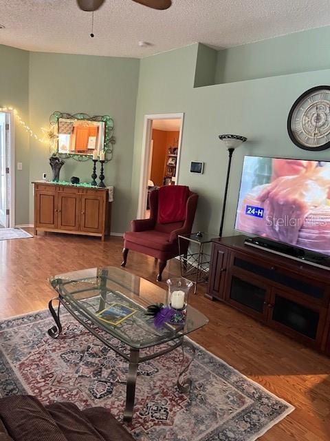 living room with lofted ceiling, a textured ceiling, a ceiling fan, and light wood finished floors