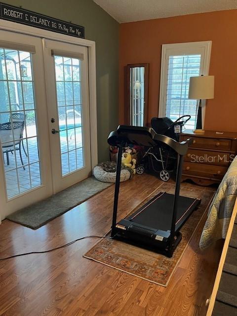 exercise room featuring french doors, wood finished floors, and vaulted ceiling