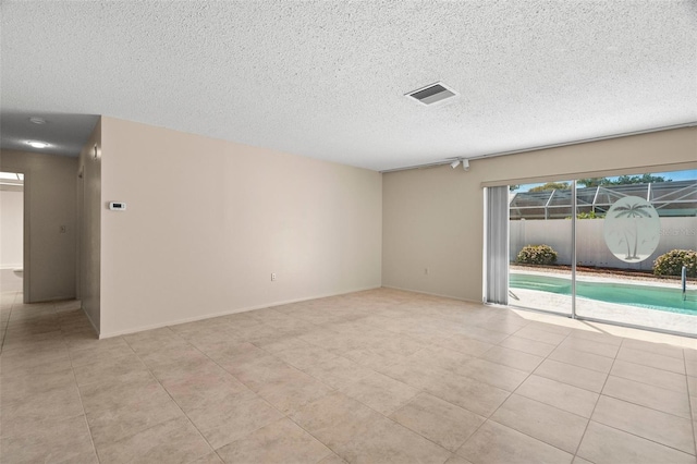 spare room with light tile patterned floors, visible vents, baseboards, and a textured ceiling