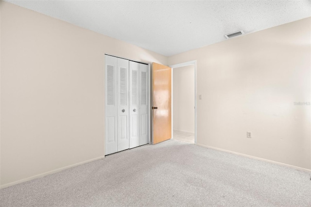 unfurnished bedroom featuring visible vents, baseboards, light colored carpet, a closet, and a textured ceiling