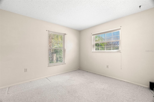 carpeted spare room featuring plenty of natural light, a textured ceiling, and baseboards