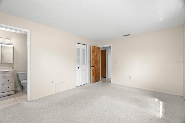 unfurnished bedroom with connected bathroom, light colored carpet, visible vents, and a closet