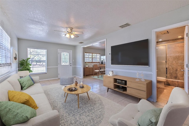 living room with ceiling fan, visible vents, a textured ceiling, and light tile patterned flooring