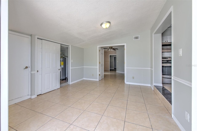 interior space with visible vents, water heater, light tile patterned flooring, a textured ceiling, and a ceiling fan