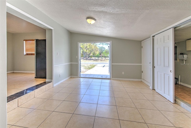 spare room with vaulted ceiling, light tile patterned floors, baseboards, and a textured ceiling