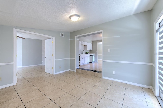 empty room with light tile patterned floors, baseboards, visible vents, and a sink