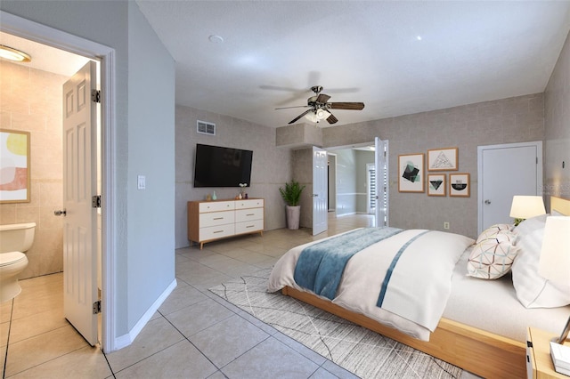 bedroom featuring light tile patterned floors, baseboards, visible vents, ensuite bathroom, and tile walls