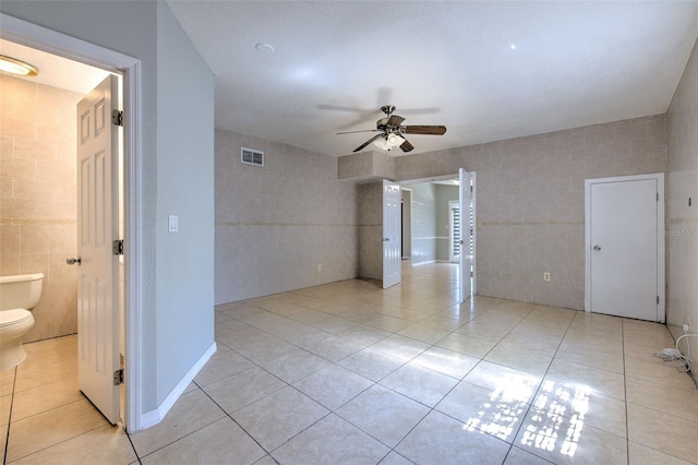 spare room featuring tile walls, light tile patterned floors, a ceiling fan, and visible vents