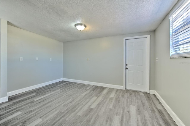 unfurnished room featuring light wood finished floors, a textured ceiling, and baseboards