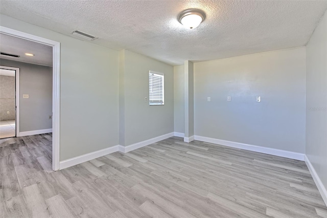 unfurnished room featuring light wood-style flooring, baseboards, visible vents, and a textured ceiling