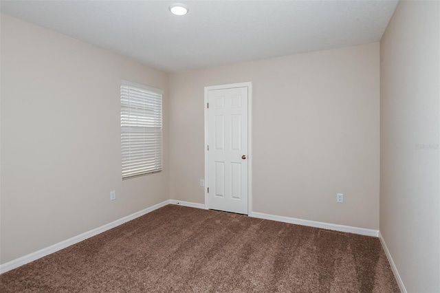 spare room with dark colored carpet and baseboards