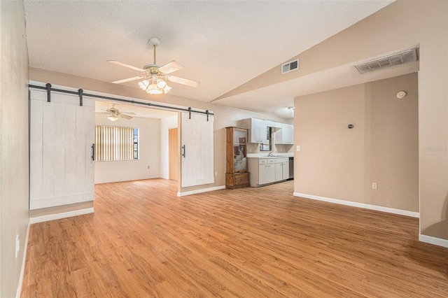 unfurnished living room with a barn door, vaulted ceiling, visible vents, and ceiling fan