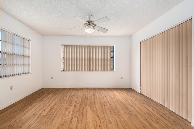 spare room featuring baseboards, light wood-style flooring, a textured ceiling, and a ceiling fan