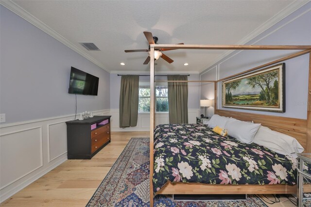 bedroom featuring visible vents, a wainscoted wall, light wood-style flooring, ornamental molding, and a decorative wall