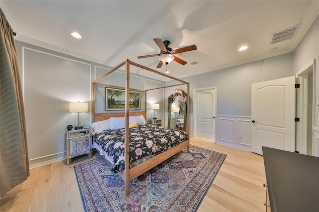 bedroom featuring visible vents, light wood finished floors, ornamental molding, and a decorative wall