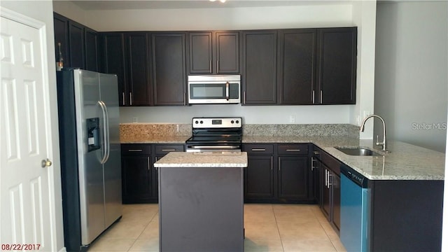 kitchen with a sink, light stone counters, a center island, appliances with stainless steel finishes, and light tile patterned floors