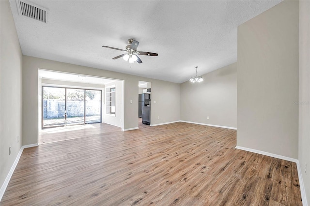 unfurnished living room with visible vents, baseboards, light wood-style flooring, ceiling fan with notable chandelier, and a textured ceiling