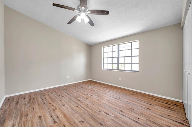 empty room with lofted ceiling, wood finished floors, baseboards, and a textured ceiling