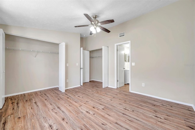 unfurnished bedroom featuring visible vents, two closets, a textured ceiling, wood finished floors, and baseboards